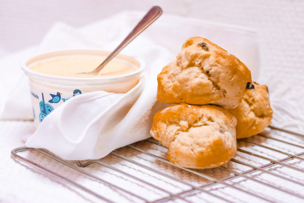A picture of some traditional Cornish scones. They are pictured with a pot of clotted cream and are ready to be eaten on a family picnic in Cornwall. 