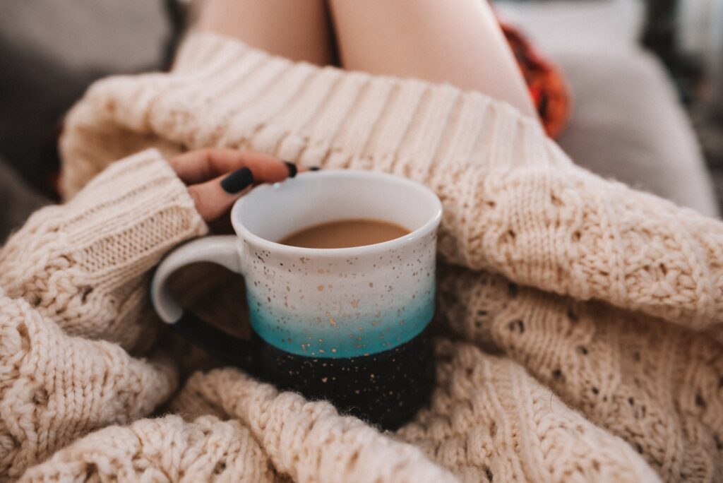 A photography of a woman in a warm, cosy sweater dress with a cup of hot tea. 