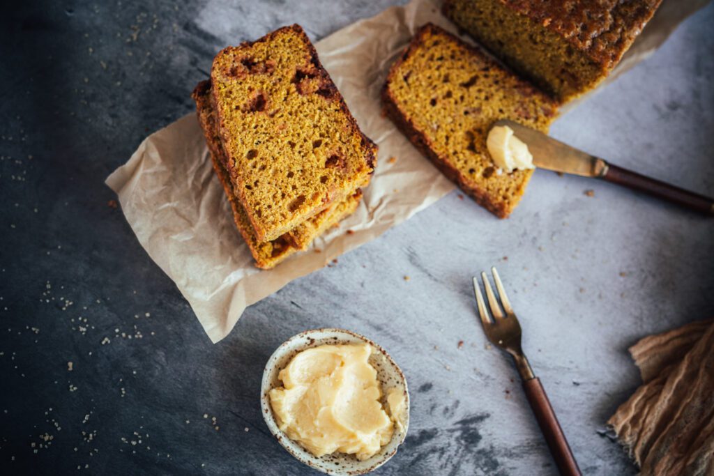 A photo of pumpkin bread sliced up with butter. It looks homemade and delicious 