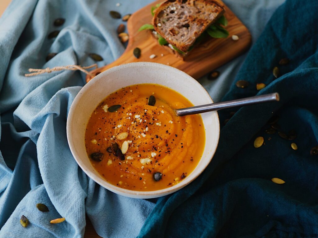 A photograph of a delicious looking bowl of fresh and homemade pumpkin soup and bread. 